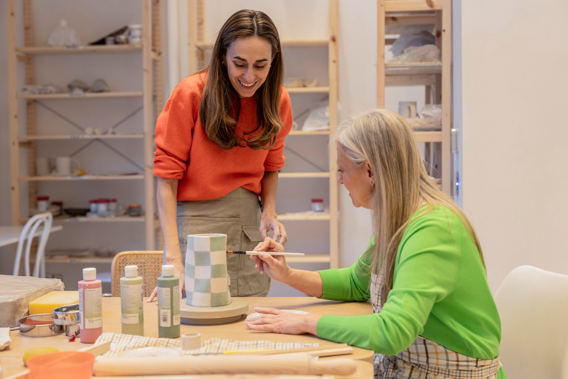 senior woman in a ceramic workshop painting while her teacher teaches her how to do it