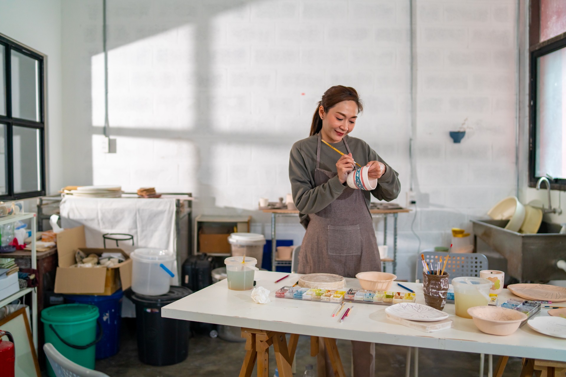 Asian woman enjoy painting self-made pottery at pottery workshop studio.